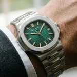 Ceas de lux cu cadran verde smarald și brățară din oțel, purtat la un costum gri elegant.